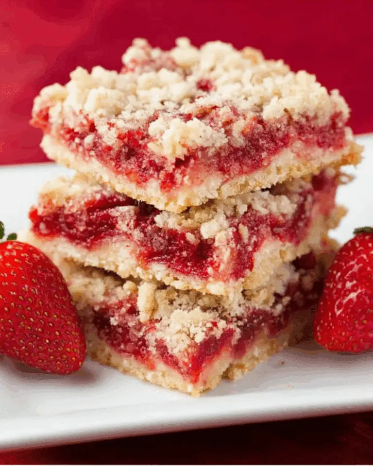Stack of Strawberry Crumb Bars on a white plate with fresh strawberries on the side.