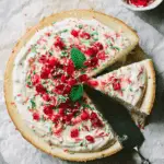 Sugar Cookie Cheesecake topped with whipped cream, festive sprinkles, red candy pieces, and fresh mint leaves.