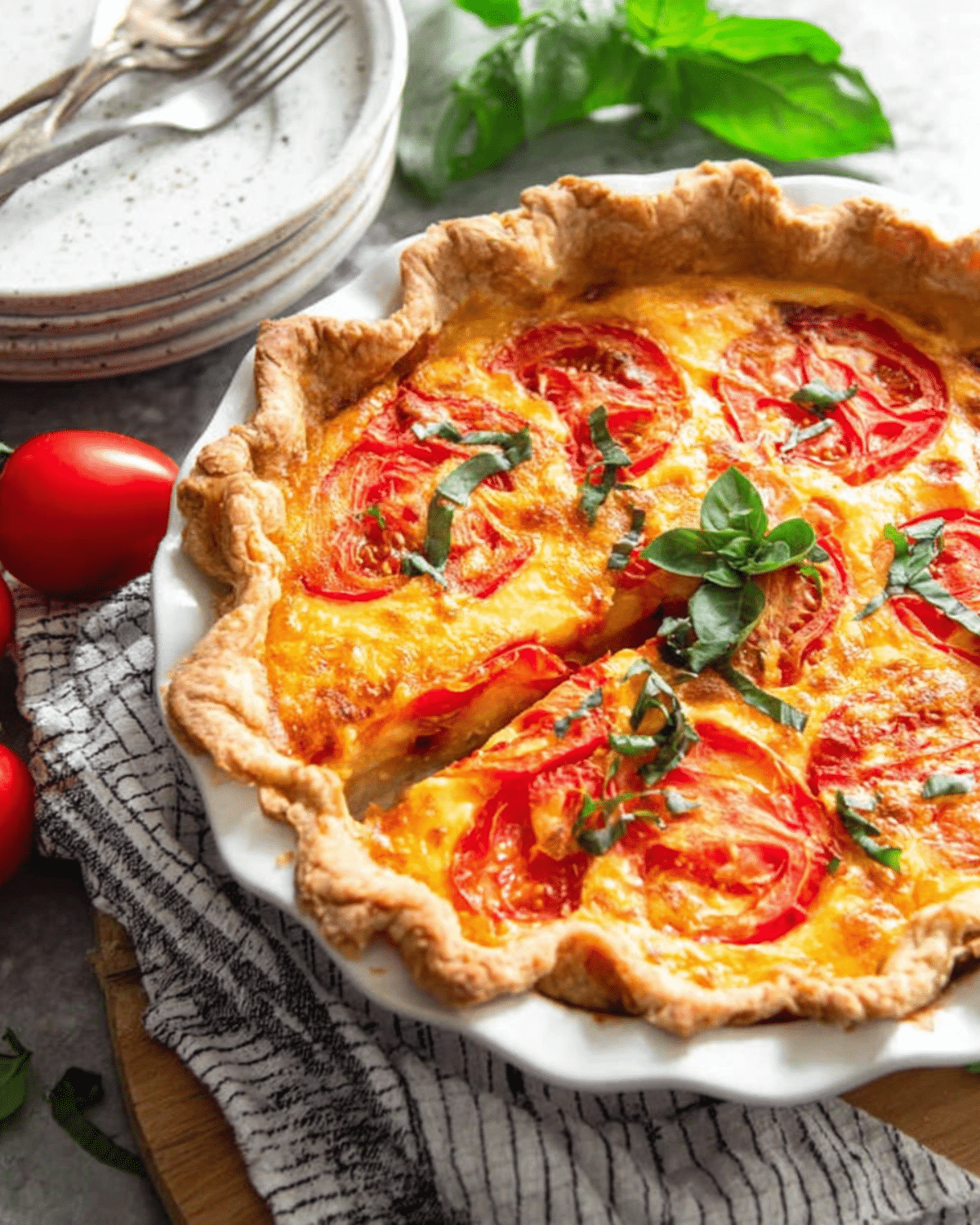 A freshly baked Southern tomato pie with a golden crust, topped with sliced tomatoes, melted cheese, and fresh basil in a white pie dish.