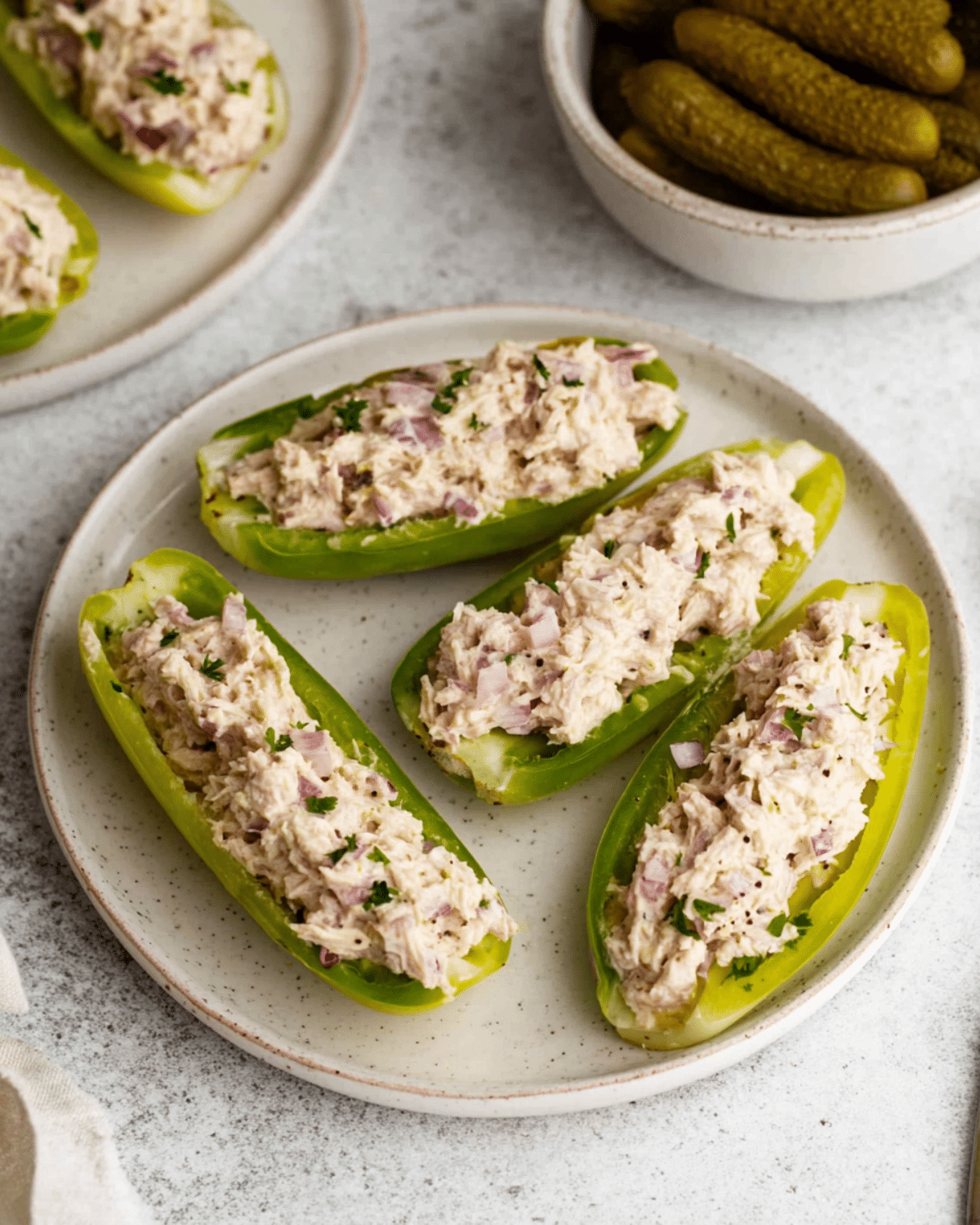 Tuna Salad Boats served in halved green bell peppers, garnished with chopped red onions and herbs on a ceramic plate.