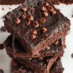 A stack of rich, fudgy 3 Ingredient Brownies topped with chocolate chips on a white parchment surface.