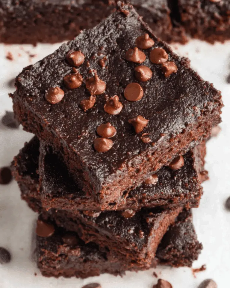 A stack of rich, fudgy 3 Ingredient Brownies topped with chocolate chips on a white parchment surface.