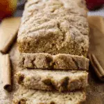 Close-up of sliced Apple Cider Donut Quick Bread on a wooden board with cinnamon sticks.
