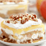 A slice of Apple Delight dessert with layers of whipped cream, apple filling, pudding, and a nutty crust topped with pecans.