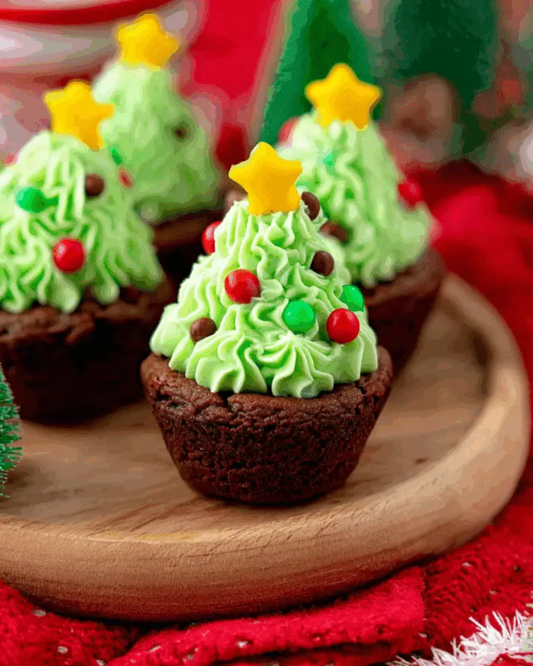 Festive Brownie Cups Christmas Tree desserts topped with green frosting, candy ornaments, and yellow star toppers, served on a wooden plate.
