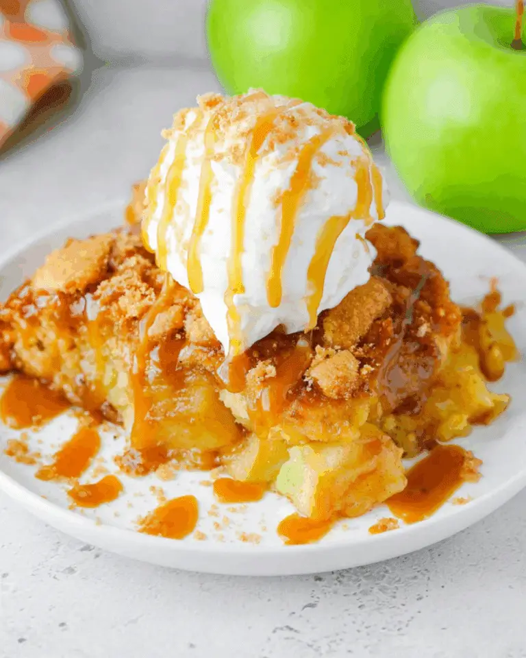 A slice of CARAMEL APPLE DUMP CAKE topped with whipped cream and drizzled caramel sauce on a white plate.