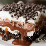 A decadent slice of CHOCOLATE LASAGNA layered with whipped cream, chocolate pudding, caramel, and chocolate chips on a white plate.