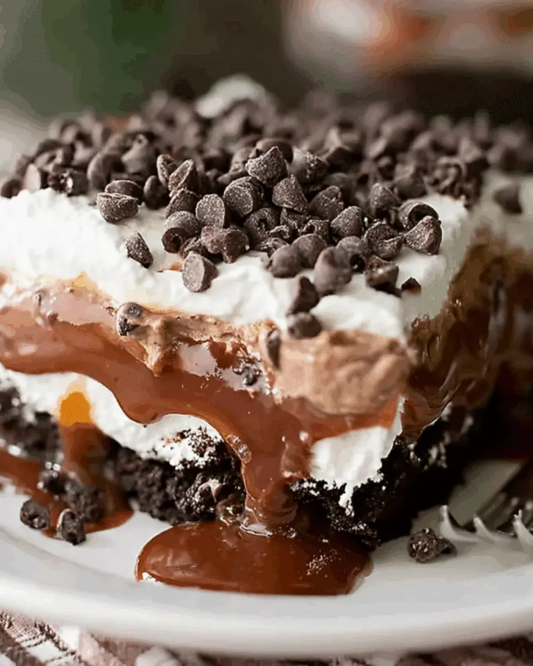 A decadent slice of CHOCOLATE LASAGNA layered with whipped cream, chocolate pudding, caramel, and chocolate chips on a white plate.