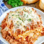 A hearty serving of crockpot lasagna topped with melted cheese and sprinkled with fresh parsley on a white plate.