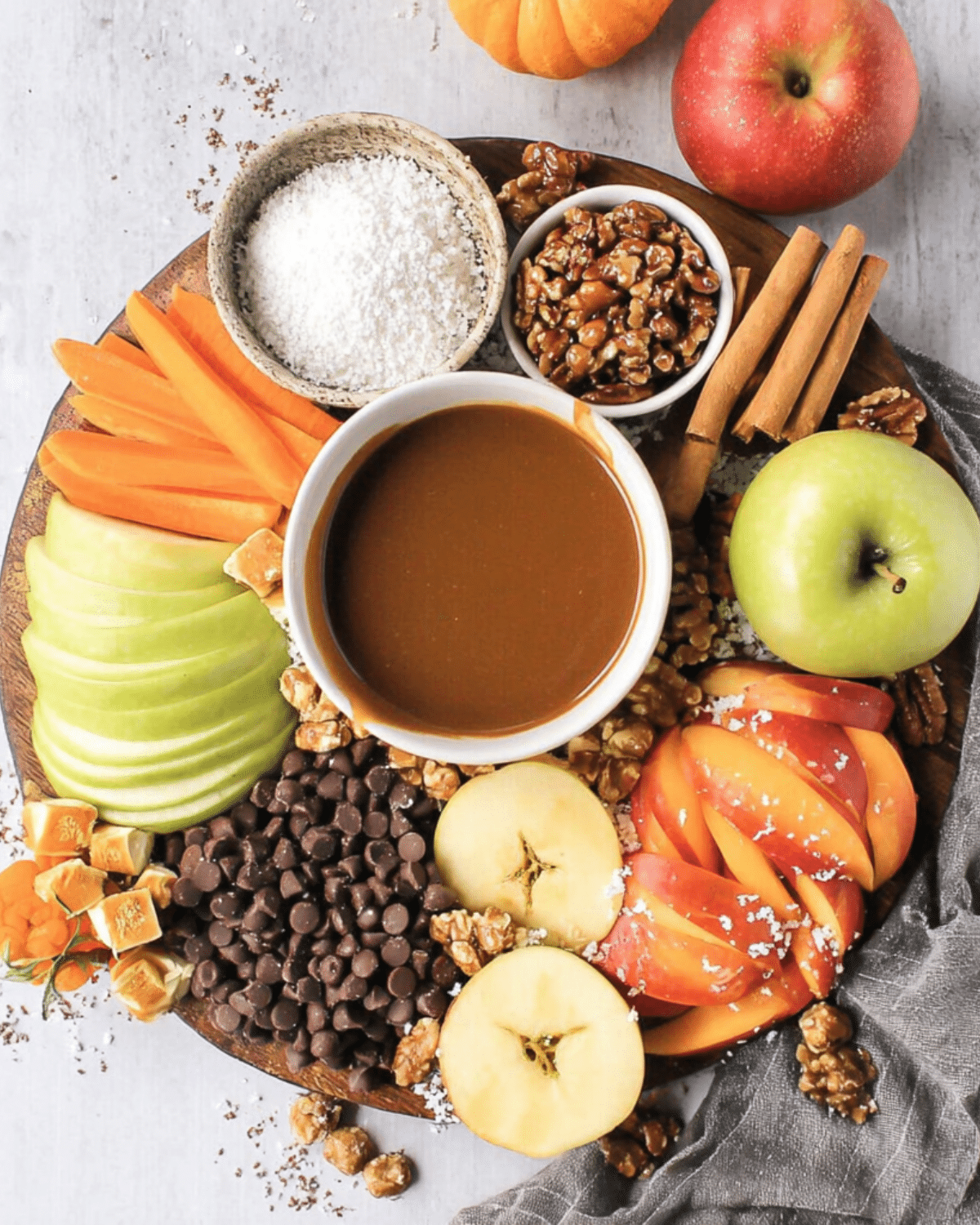 A festive Caramel Apple Dip Board with sliced apples, chocolate chips, caramel candies, nuts, shredded coconut, and a bowl of caramel dip.