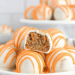Carrot cake cheesecake bites coated in white chocolate with orange drizzle, one cut open to show the moist carrot cake filling inside.