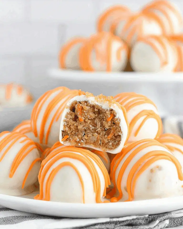 Carrot cake cheesecake bites coated in white chocolate with orange drizzle, one cut open to show the moist carrot cake filling inside.