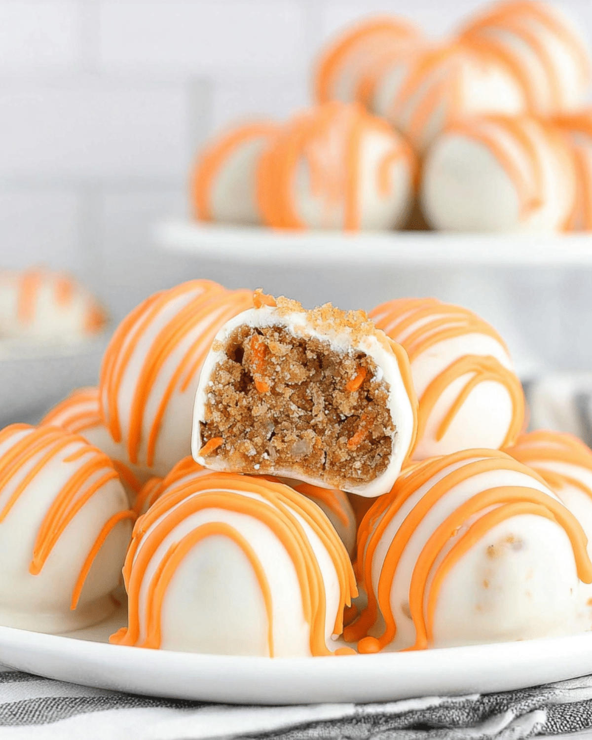 Carrot cake cheesecake bites coated in white chocolate with orange drizzle, one cut open to show the moist carrot cake filling inside.
