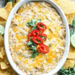 Cheesy Chicken Fajita Dip topped with red chili slices and cilantro, served with tortilla chips and lime wedges.