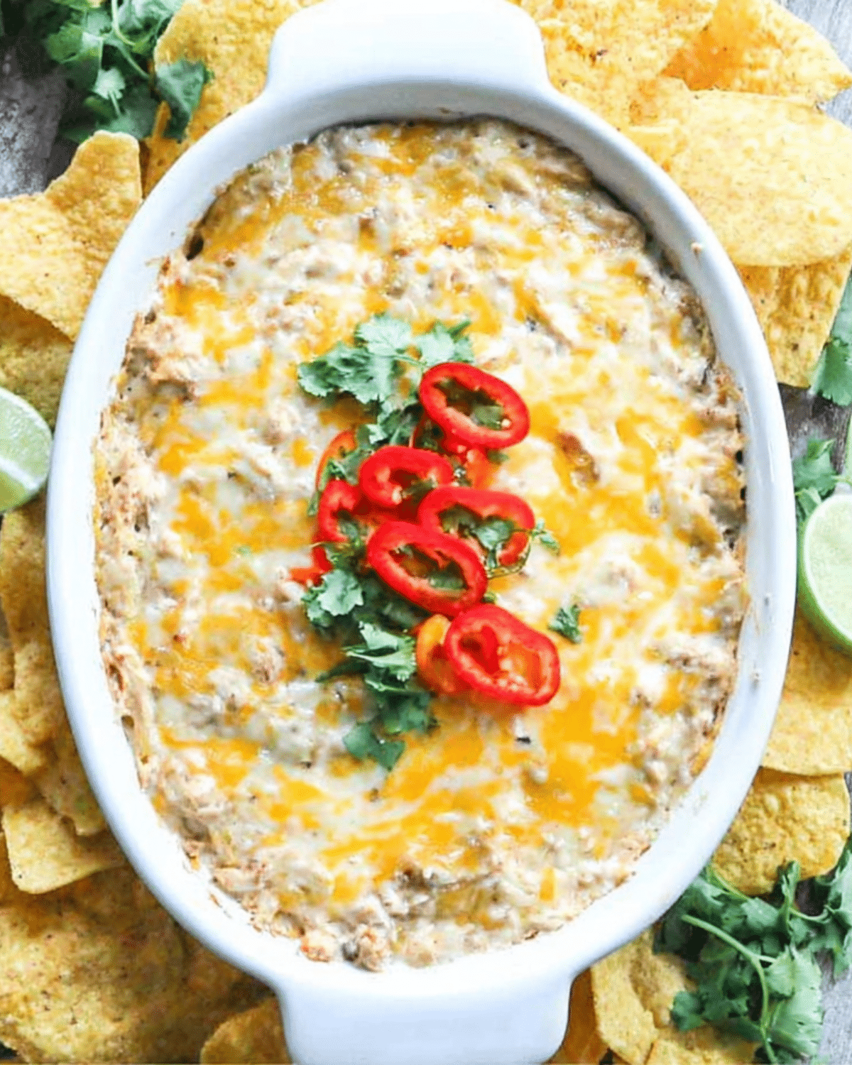 Cheesy Chicken Fajita Dip topped with red chili slices and cilantro, served with tortilla chips and lime wedges.