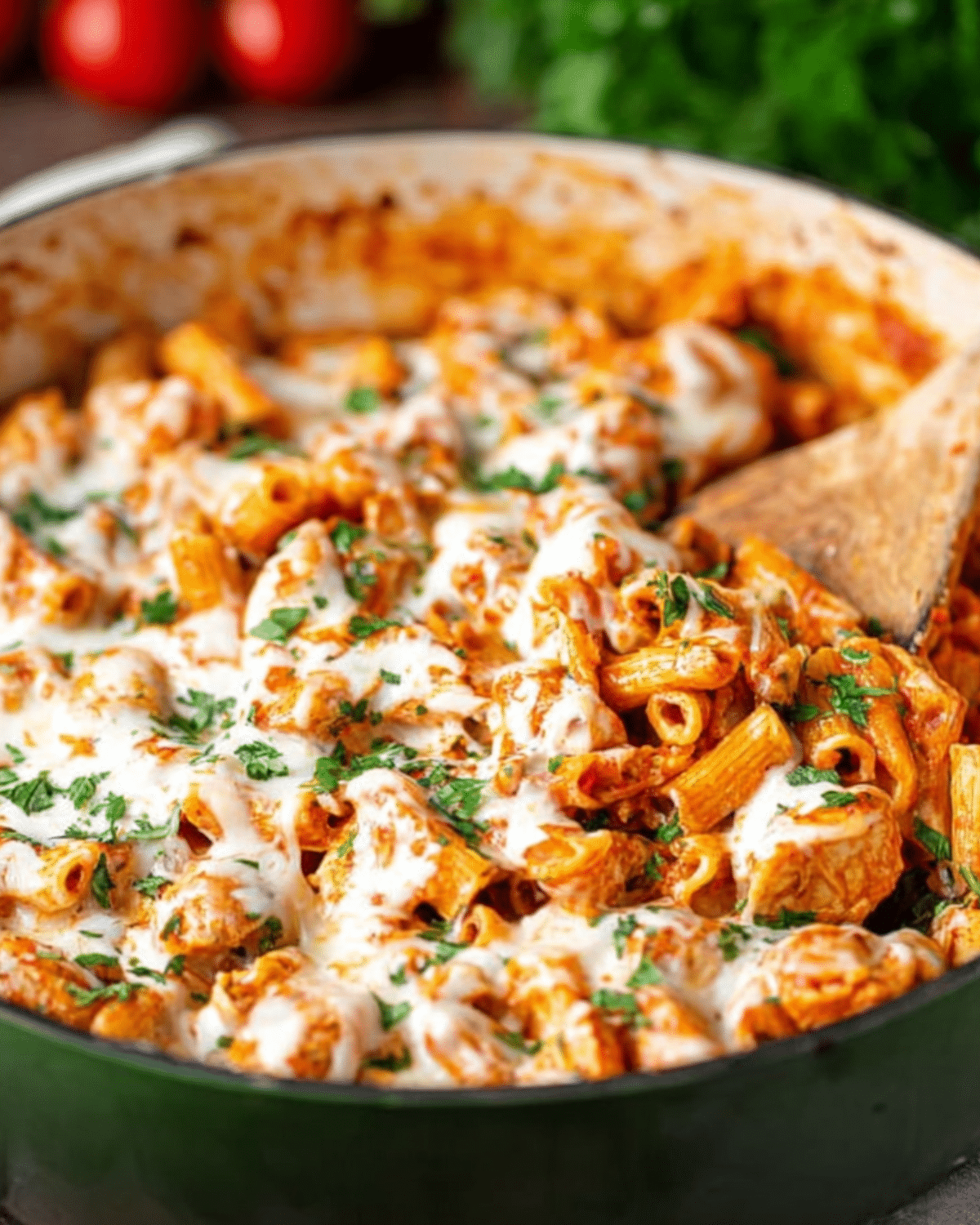 A skillet filled with cheesy chicken parmesan pasta, featuring rigatoni, marinara sauce, melted mozzarella, and fresh parsley.