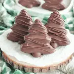 Chocolate peanut butter Christmas trees drizzled with melted chocolate, displayed on parchment paper over a wooden board.