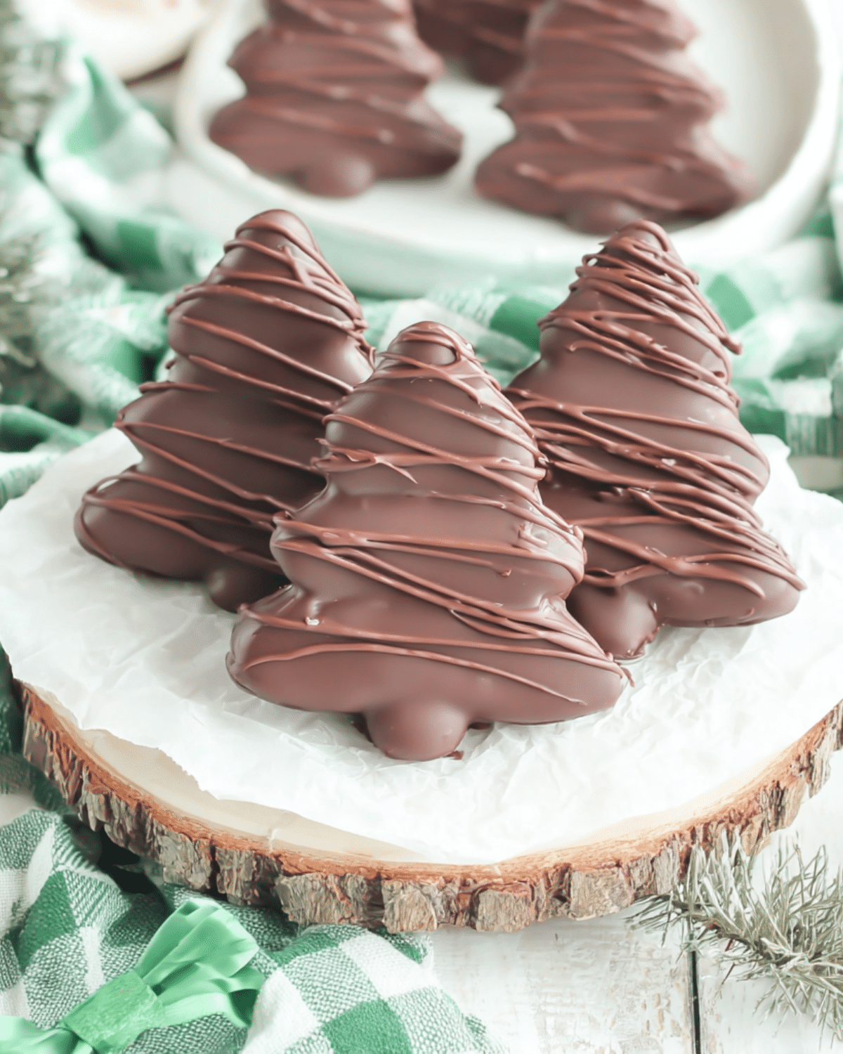 Chocolate peanut butter Christmas trees drizzled with melted chocolate, displayed on parchment paper over a wooden board.
