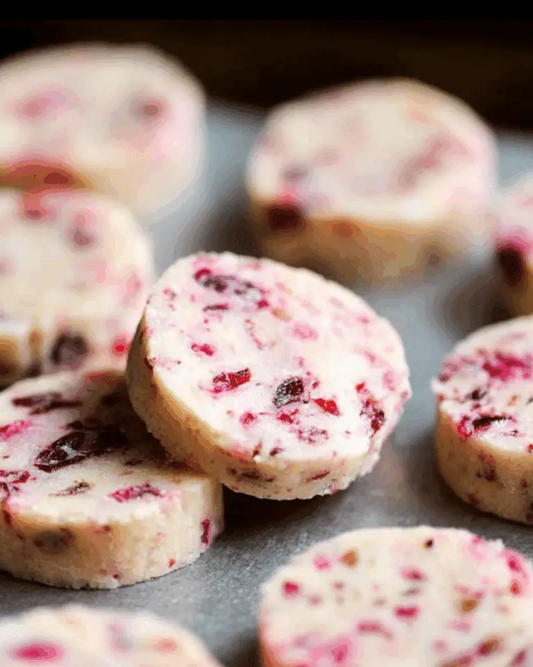 Round slices of Cranberry Shortbread Cookies with specks of red cranberries on a baking sheet.