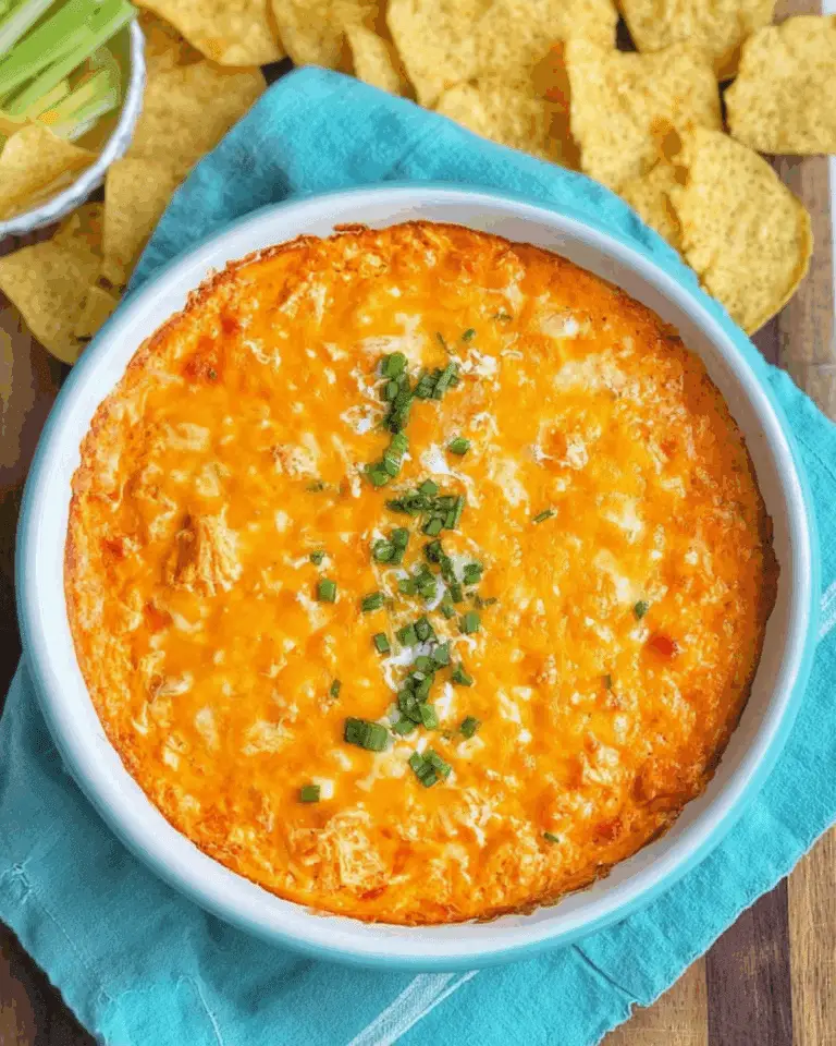Creamy Cheesy Buffalo Chicken Dip in a white baking dish, topped with melted cheese and chopped green onions, served with tortilla chips and celery sticks.