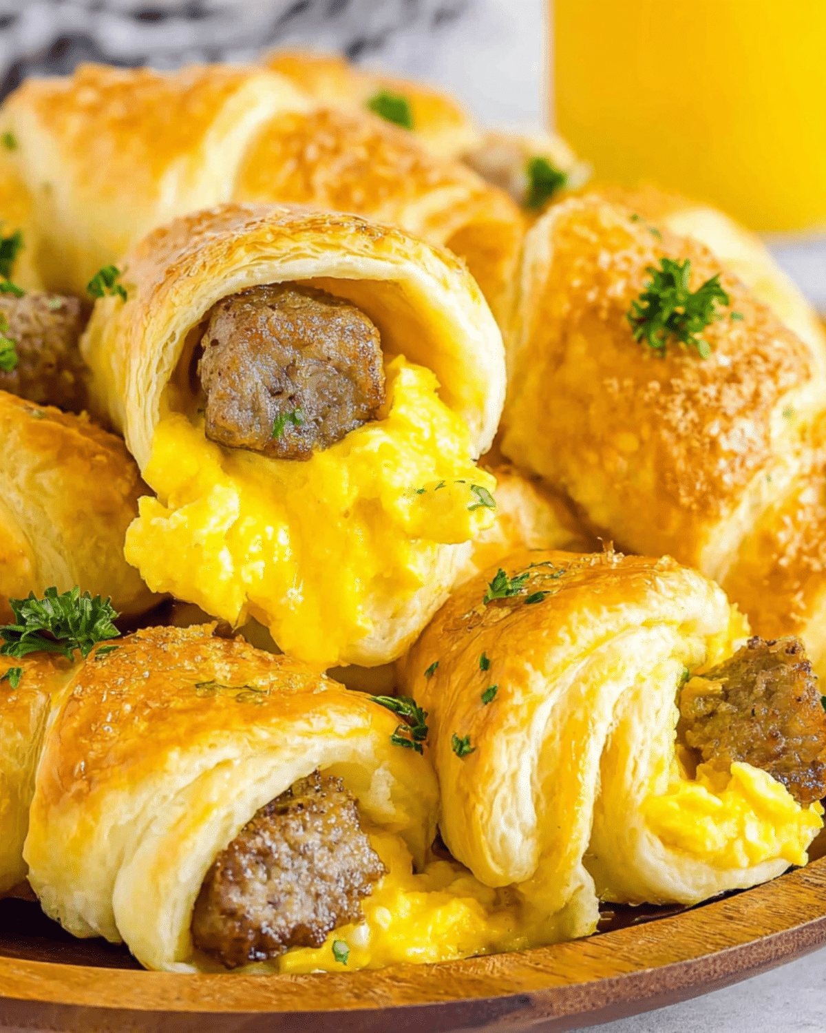 Golden Crescent Roll Breakfast stuffed with scrambled eggs, sausage, and cheese, garnished with parsley on a wooden plate.