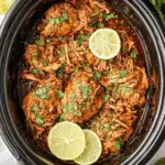 Crockpot Cilantro Lime Chicken with shredded chicken breasts garnished with fresh cilantro and lime slices in a slow cooker.