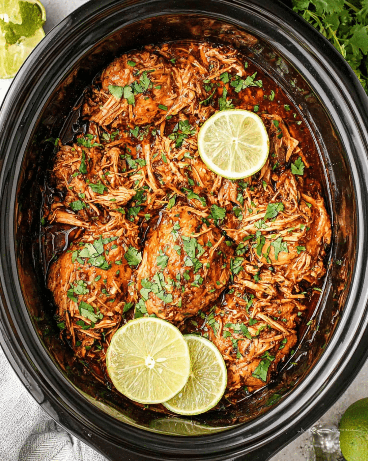 Crockpot Cilantro Lime Chicken with shredded chicken breasts garnished with fresh cilantro and lime slices in a slow cooker.