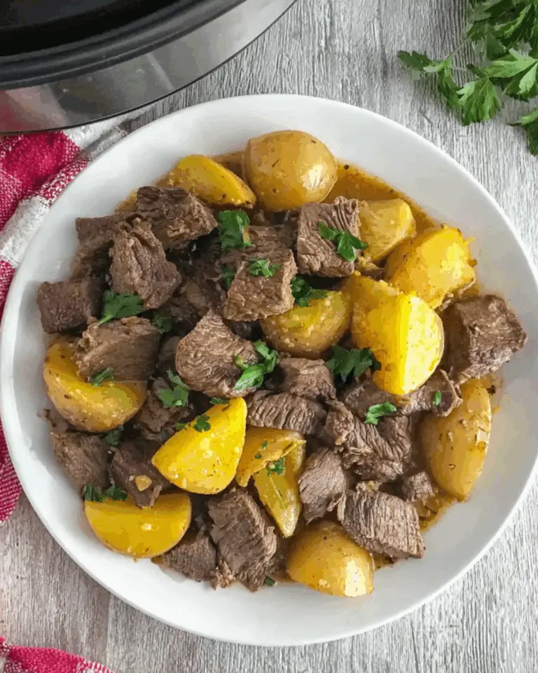 Crockpot Garlic Butter Beef Bites with Potatoes served on a white plate, garnished with fresh parsley.