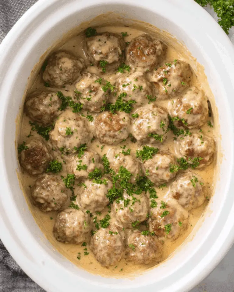 Crockpot Swedish meatballs in a creamy gravy sauce, garnished with fresh parsley inside a white slow cooker.