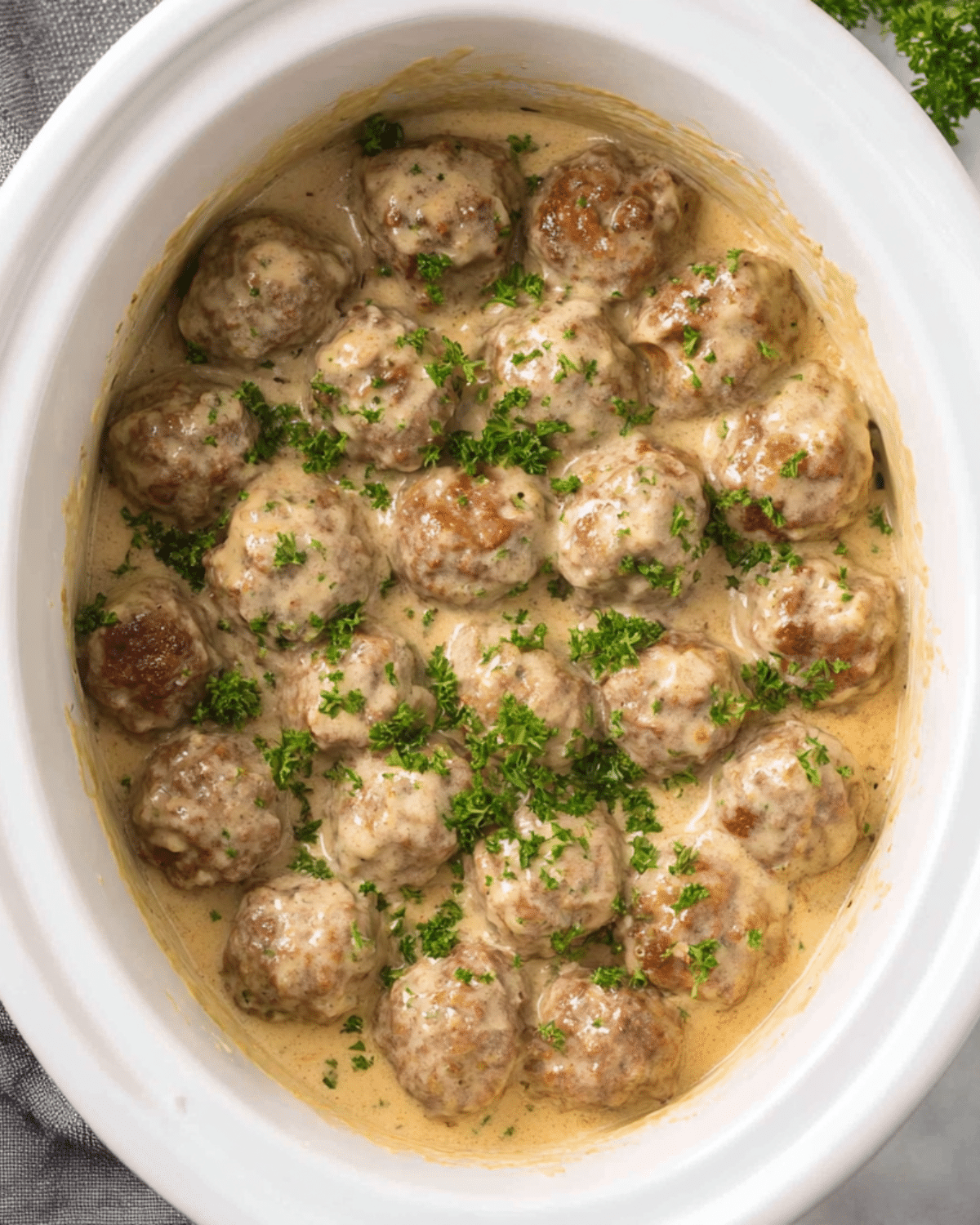 Crockpot Swedish meatballs in a creamy gravy sauce, garnished with fresh parsley inside a white slow cooker.