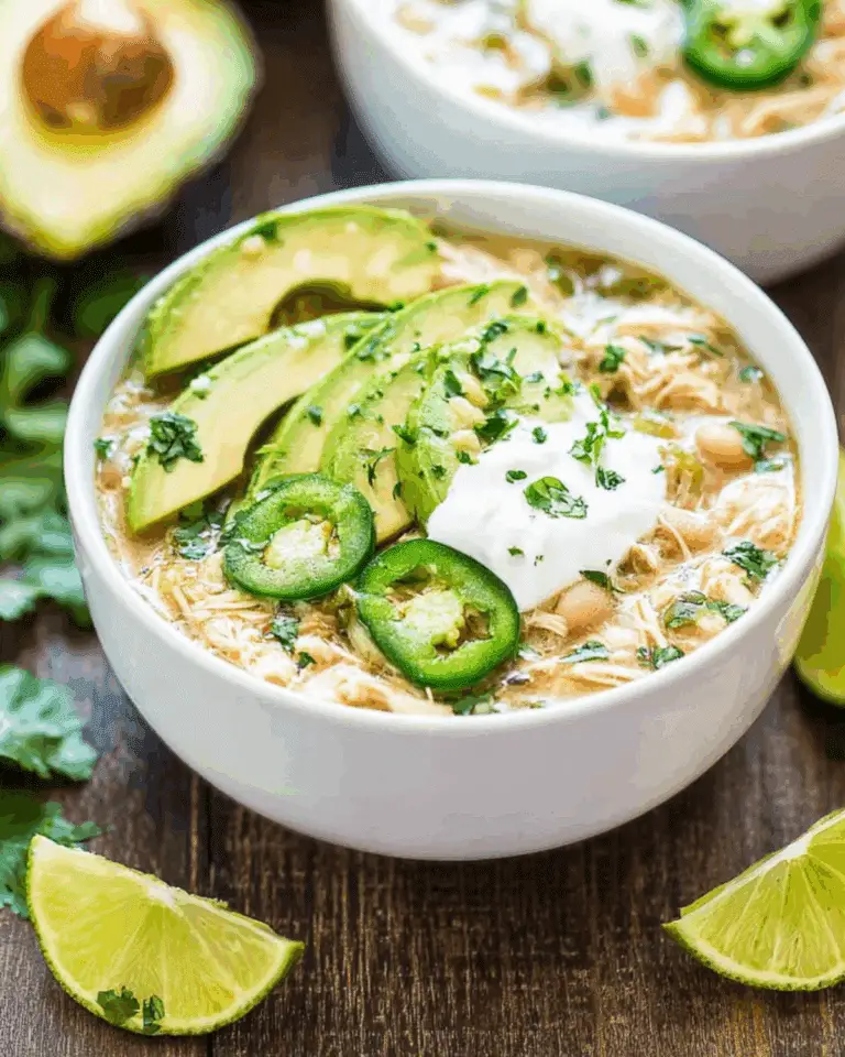 A bowl of Crockpot White Chicken Chili topped with sliced avocado, jalapeños, sour cream, and chopped cilantro.