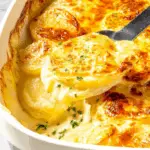 Easy cheesy scalloped potatoes in a casserole dish with a golden, bubbly top being scooped out.