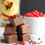 Stacked cubes of creamy Fireball Fudge garnished with red candies and chocolate bits, with a bottle of Fireball whiskey in the background.