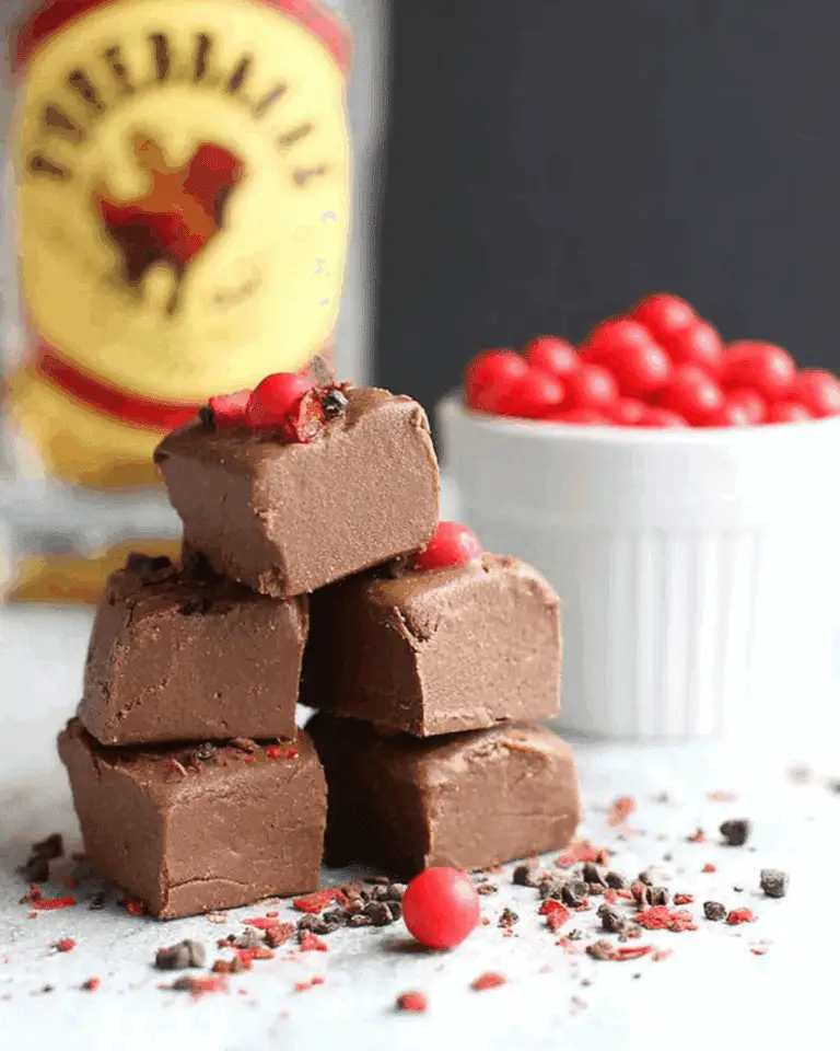 Stacked cubes of creamy Fireball Fudge garnished with red candies and chocolate bits, with a bottle of Fireball whiskey in the background.