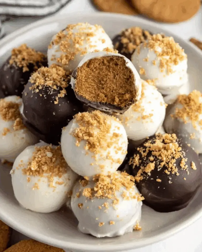 Plate of gingerbread truffles coated in white and dark chocolate, sprinkled with cookie crumbs, with one truffle cut open to reveal a spiced gingerbread filling.