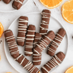 Plates of Homemade Chocolate Orange Sticks drizzled with white chocolate, surrounded by fresh orange slices.