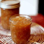 A jar of Homemade Spiced Honey Pear Jam with a golden-brown color, set on a cooling rack.