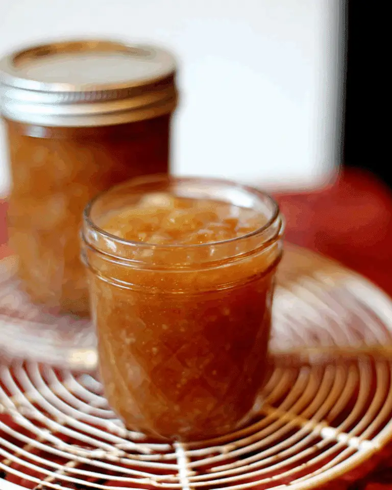 A jar of Homemade Spiced Honey Pear Jam with a golden-brown color, set on a cooling rack.