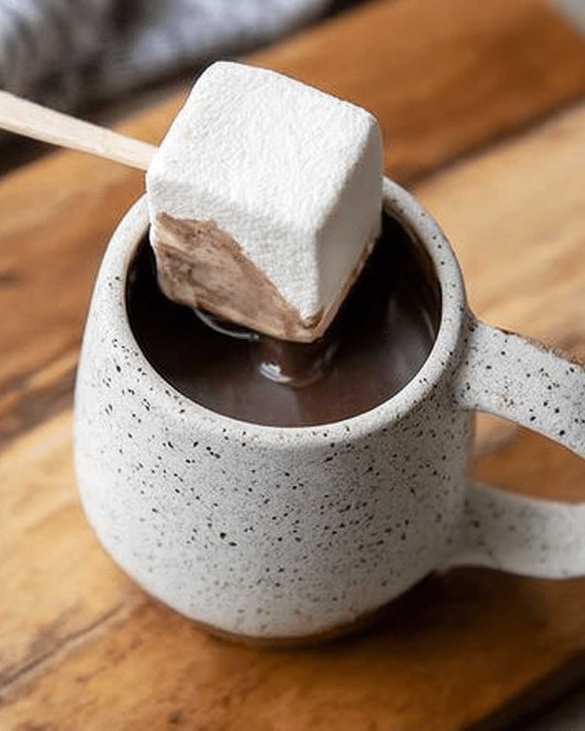 Hot chocolate on a stick with a large square marshmallow dipped into a mug of rich, creamy hot cocoa.