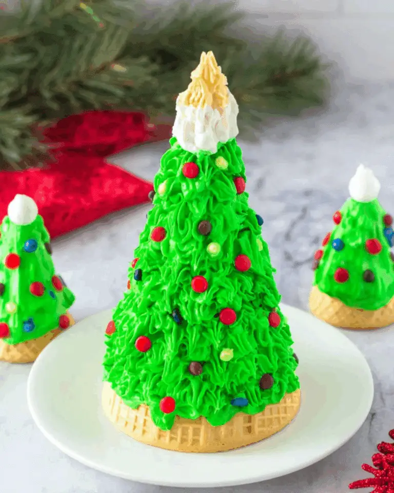 Festive Ice Cream Cone Christmas Tree decorated with green frosting, colorful candies, and a whipped cream topper, displayed on a white plate.