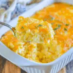 Spoonful of cheesy Jiffy corn casserole being served from a white baking dish.