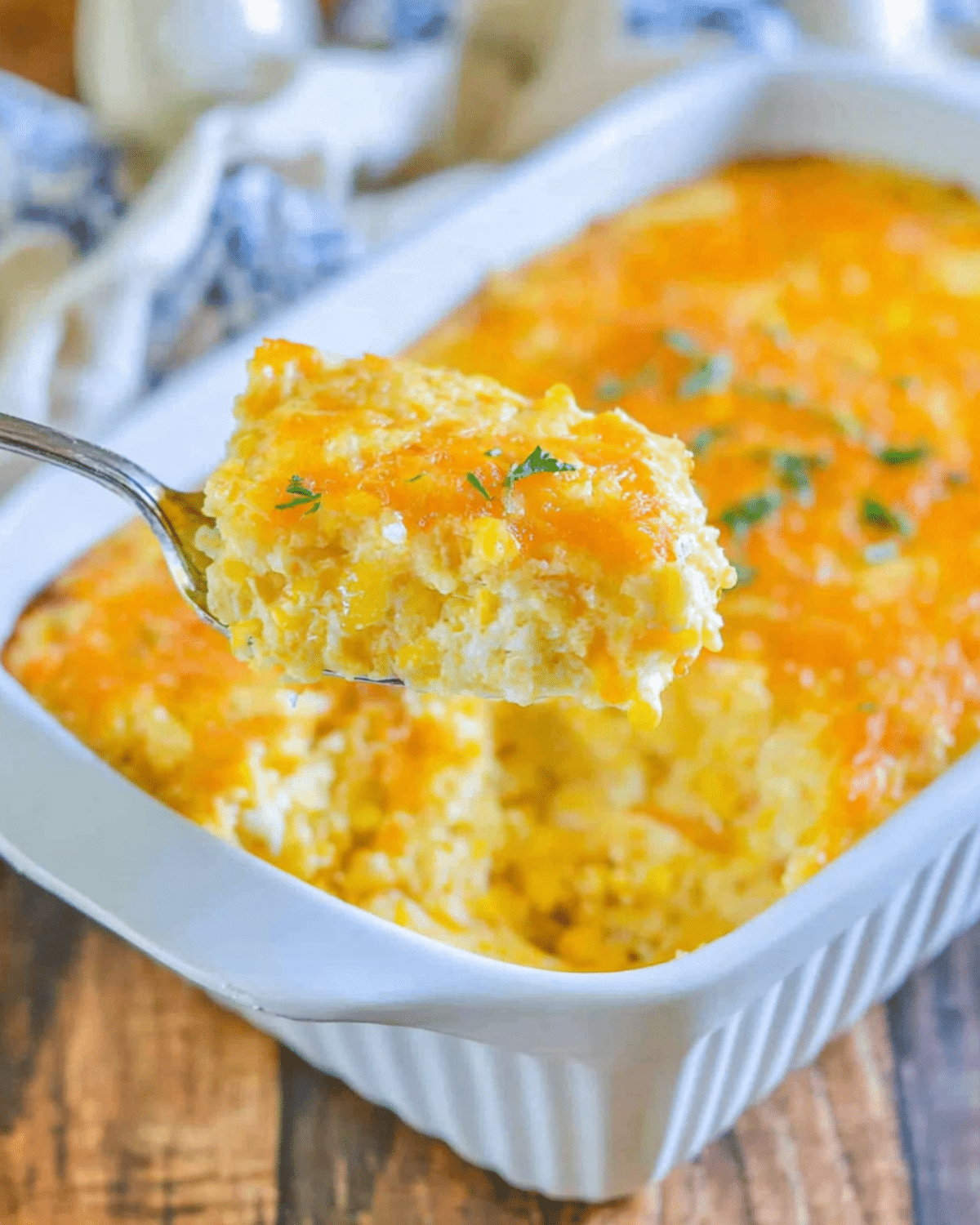 Spoonful of cheesy Jiffy corn casserole being served from a white baking dish.
