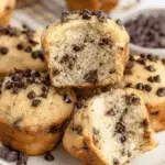 A plate of Mini Chocolate Chip Muffins, with one muffin cut open to reveal its soft, fluffy texture and chocolate chips inside.