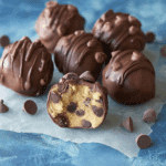 Close-up of No Bake Chocolate Chip Cookie Dough Truffles coated in chocolate, with one truffle cut open to reveal the cookie dough center filled with chocolate chips.
