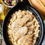 Olive Garden chicken served over creamy pasta in a slow cooker, topped with parmesan cheese and herbs.