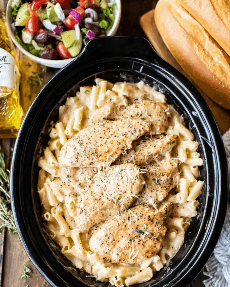 Olive Garden chicken served over creamy pasta in a slow cooker, topped with parmesan cheese and herbs.