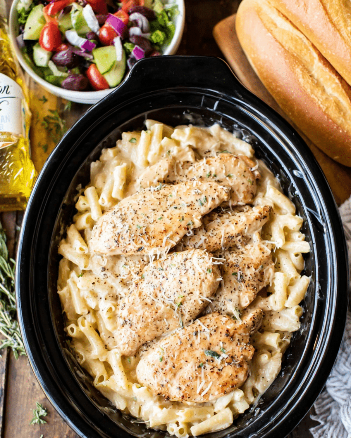 Olive Garden chicken served over creamy pasta in a slow cooker, topped with parmesan cheese and herbs.