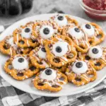 A plate of Pretzels Monster Eyeballs made with pretzels, white chocolate, and candy eyeballs topped with black centers.