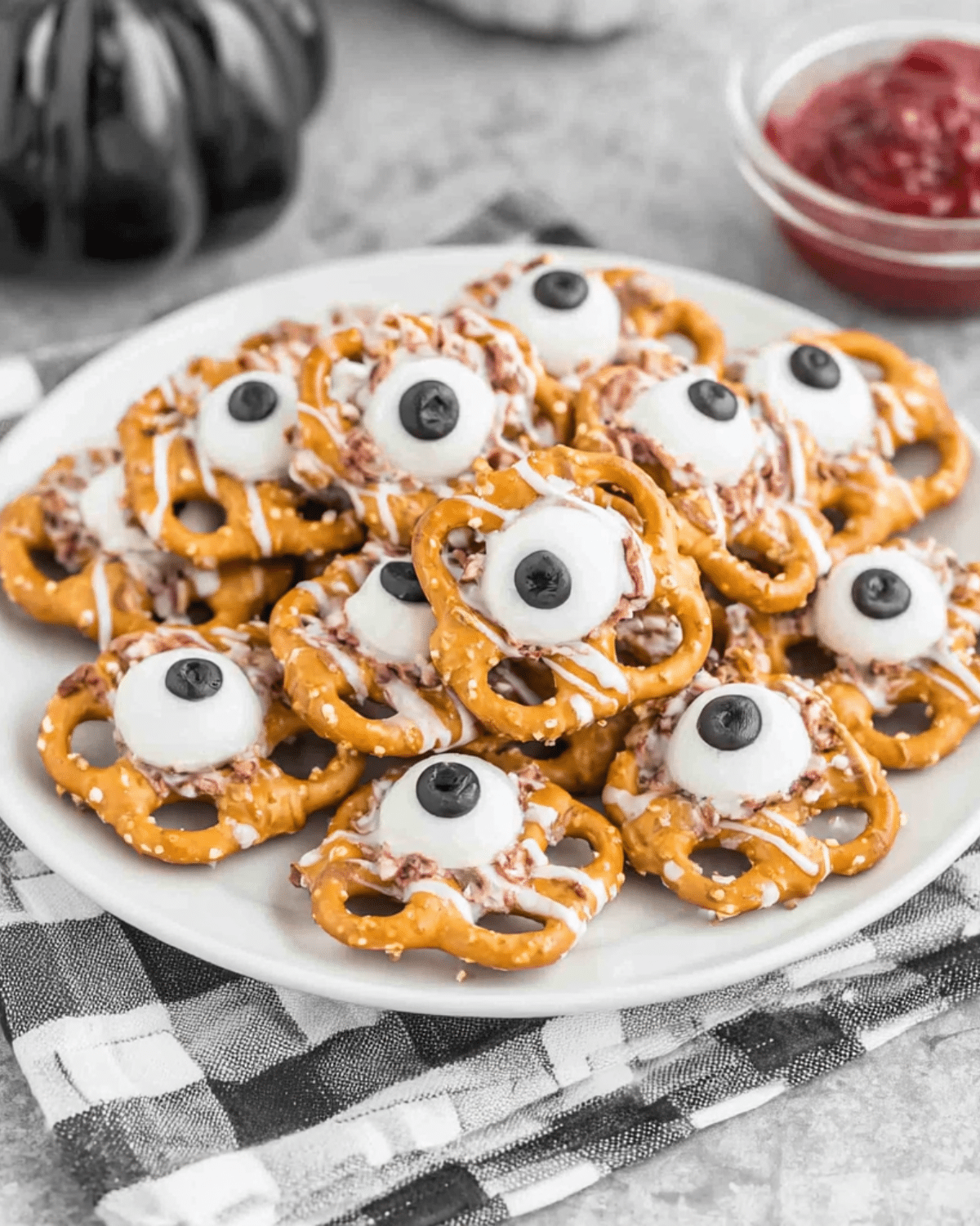 A plate of Pretzels Monster Eyeballs made with pretzels, white chocolate, and candy eyeballs topped with black centers.