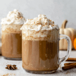 Glass mugs filled with Pumpkin Spice Latte topped with whipped cream and a sprinkle of cinnamon.